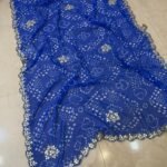 Four vibrant Bandhej sarees in red, pink, blue, and green with heavy Gota Patti borders lying on a floor.