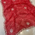 Four vibrant Bandhej sarees in red, pink, blue, and green with heavy Gota Patti borders lying on a floor.
