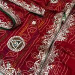 A vibrant red Bandhej georgette saree featuring detailed gold Gota Patti peacock motifs and borders.