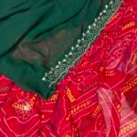 A close-up view of a red and yellow Chunari Bandhej saree with an intricate green border featuring detailed golden handwork.