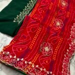 A close-up view of a red and yellow Chunari Bandhej saree with an intricate green border featuring detailed golden handwork.