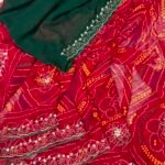 A close-up view of a red and yellow Chunari Bandhej saree with an intricate green border featuring detailed golden handwork.