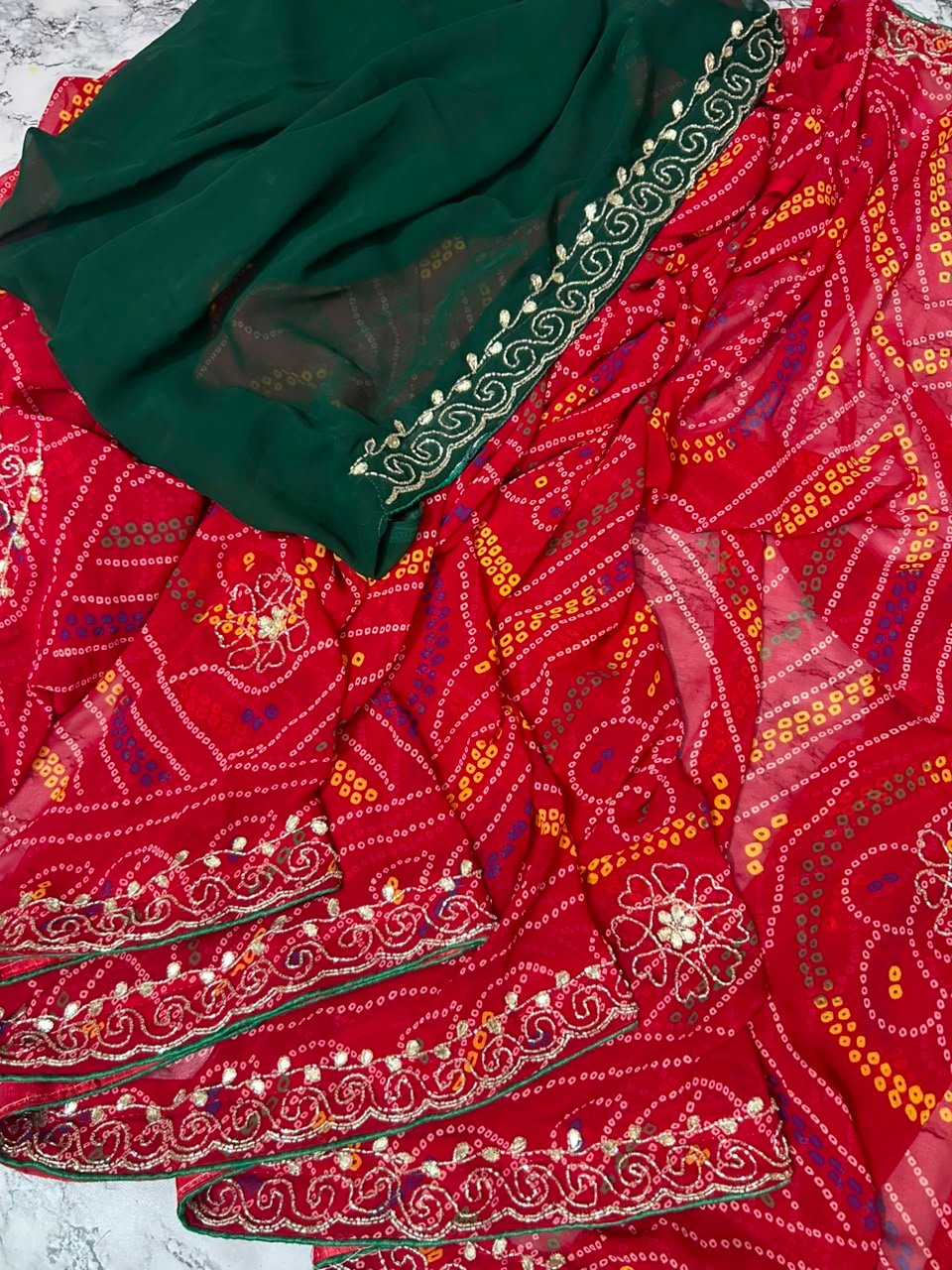 Chunari Bandhej Handwork Synthetic Georgette Saree 3 A close-up view of a red and yellow Chunari Bandhej saree with an intricate green border featuring detailed golden handwork.