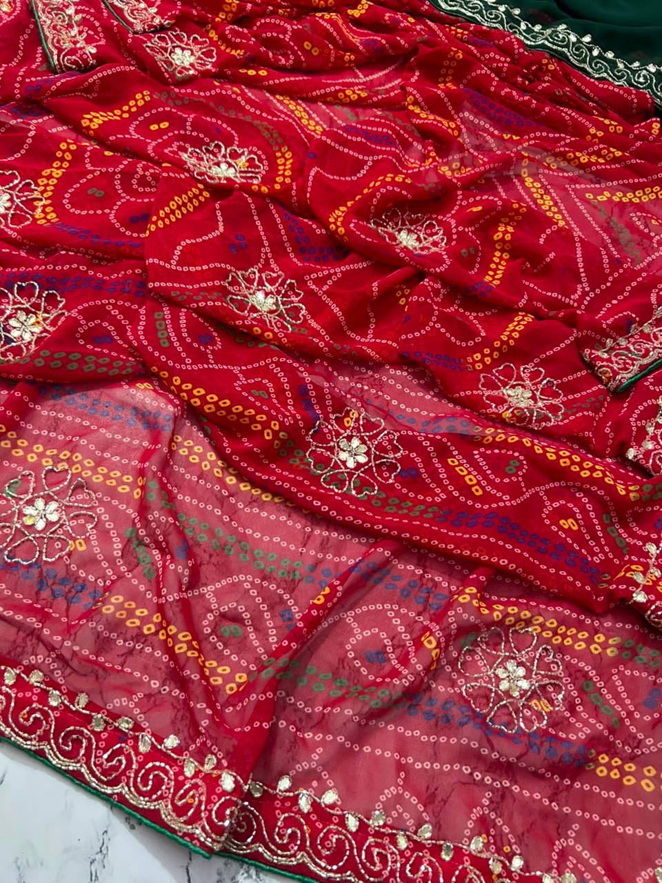 Chunari Bandhej Handwork Synthetic Georgette Saree 4 A close-up view of a red and yellow Chunari Bandhej saree with an intricate green border featuring detailed golden handwork.