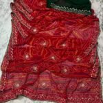 A close-up view of a red and yellow Chunari Bandhej saree with an intricate green border featuring detailed golden handwork.