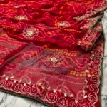 A close-up view of a red and yellow Chunari Bandhej saree with an intricate green border featuring detailed golden handwork.