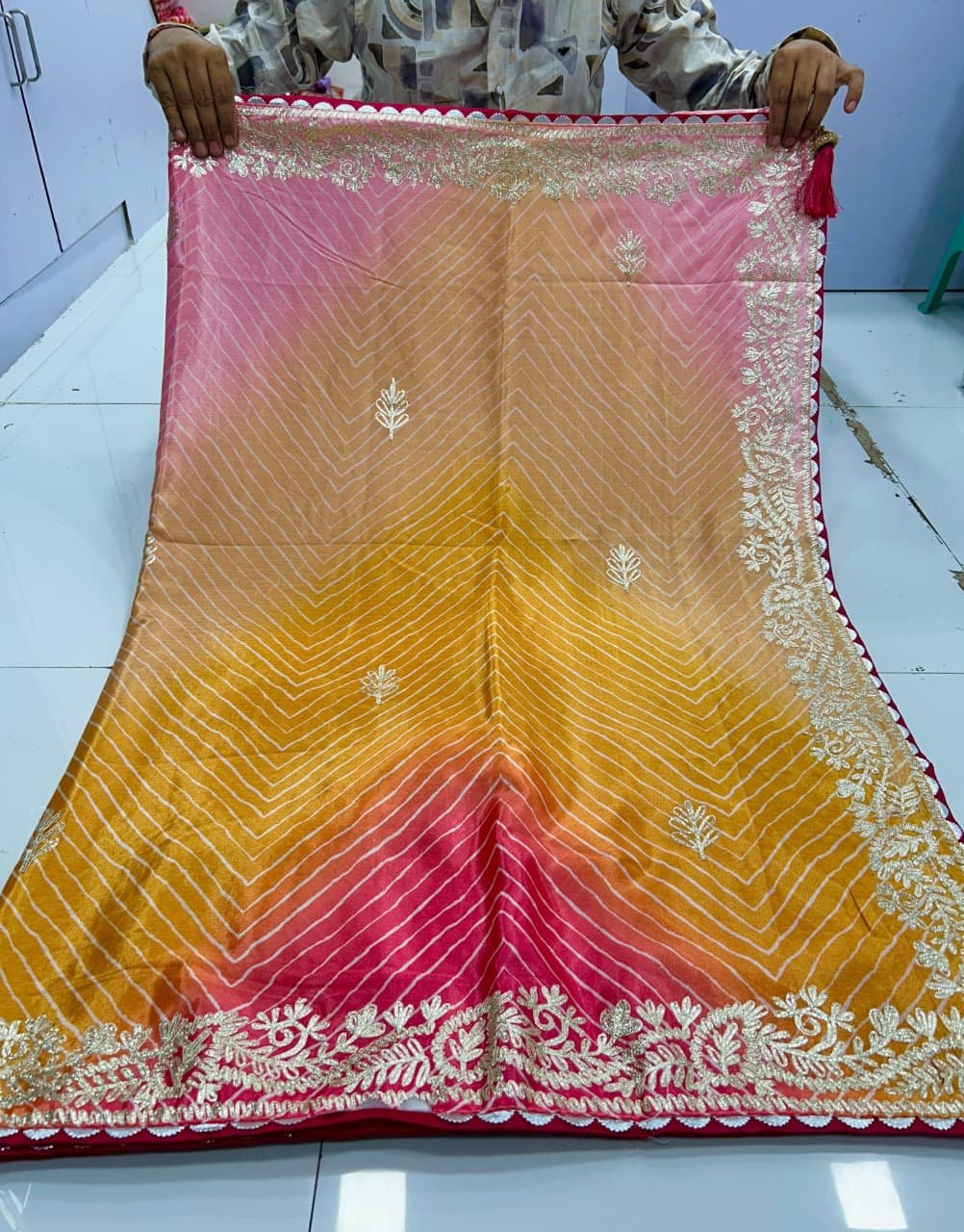 Chinnon Leheriya Saree with Ribbon Work 1 A beautiful pink and yellow gradient Leheriya saree in Chinnon fabric with intricate ribbon work border held by hands.
