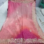 A beautiful pink and yellow gradient Leheriya saree in Chinnon fabric with intricate ribbon work border held by hands.