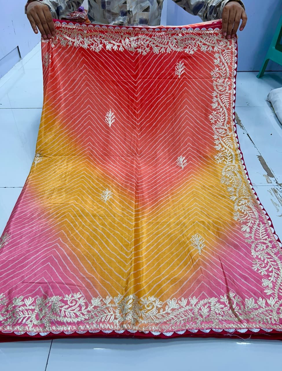 Chinnon Leheriya Saree with Ribbon Work 3 A beautiful pink and yellow gradient Leheriya saree in Chinnon fabric with intricate ribbon work border held by hands.