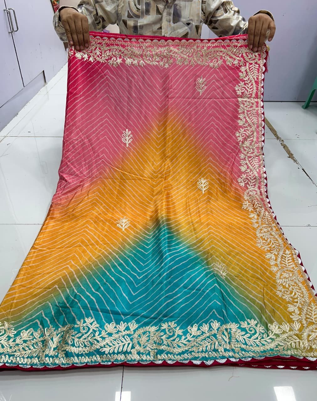 Chinnon Leheriya Saree with Ribbon Work 4 A beautiful pink and yellow gradient Leheriya saree in Chinnon fabric with intricate ribbon work border held by hands.