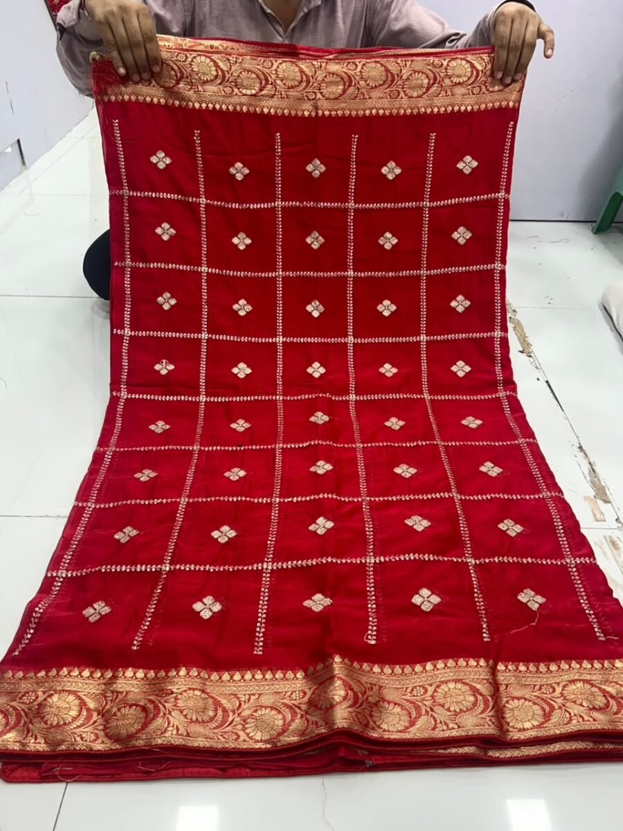 New Arrivals 38 A beautiful red Chinon saree with heavy Zari work, butti, and a golden Jacquard border, being held up to display the design.