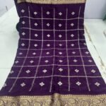 A beautiful red Chinon saree with heavy Zari work, butti, and a golden Jacquard border, being held up to display the design.