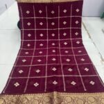 A beautiful red Chinon saree with heavy Zari work, butti, and a golden Jacquard border, being held up to display the design.