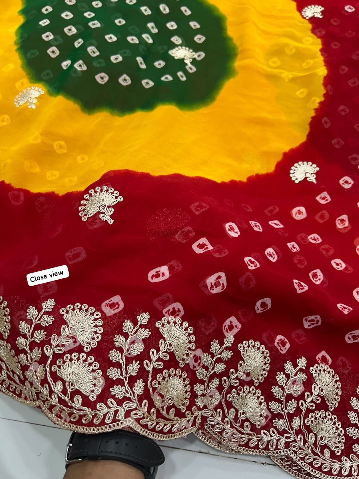 Chunri Bandhani Saree in Pure Georgette with Pita Work 4 A woman posing in the desert wearing a vibrant red, yellow, and green Chunri Bandhani saree with intricate pita work.