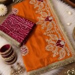 A beautiful red Cosmos silk saree featuring heavy Gota Patti work and Bandhej patches, displayed with matching bangles and earrings.