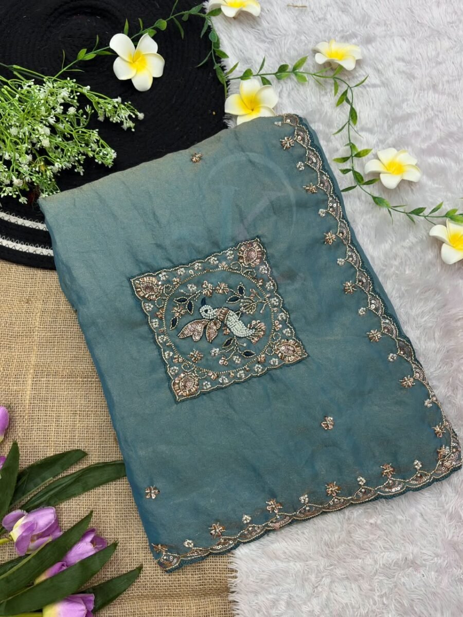 New Arrivals 26 A beautiful teal designer saree laid out flat with peacock embroidery and sequin work, surrounded by white flowers and purple tulips.