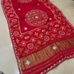 A beautiful red pure Modal Gajji Patola saree with intricate Gota Patti handwork and a metallic zari border spread across a tiled floor.