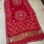 A beautiful red pure Modal Gajji Patola saree with intricate Gota Patti handwork and a metallic zari border spread across a tiled floor.