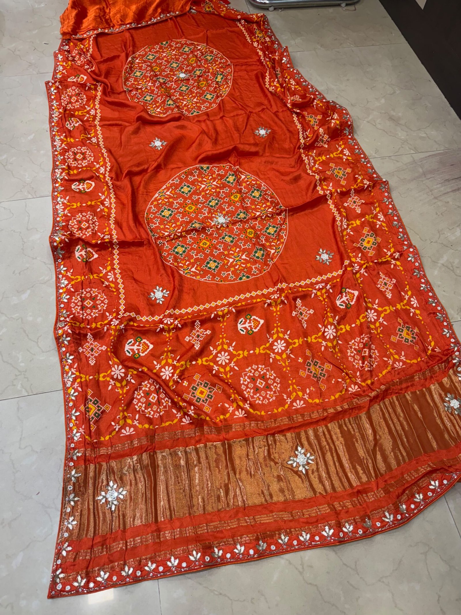 Pure Modal Gajji Patola Saree with Gota Patti Work 2 A beautiful red pure Modal Gajji Patola saree with intricate Gota Patti handwork and a metallic zari border spread across a tiled floor.