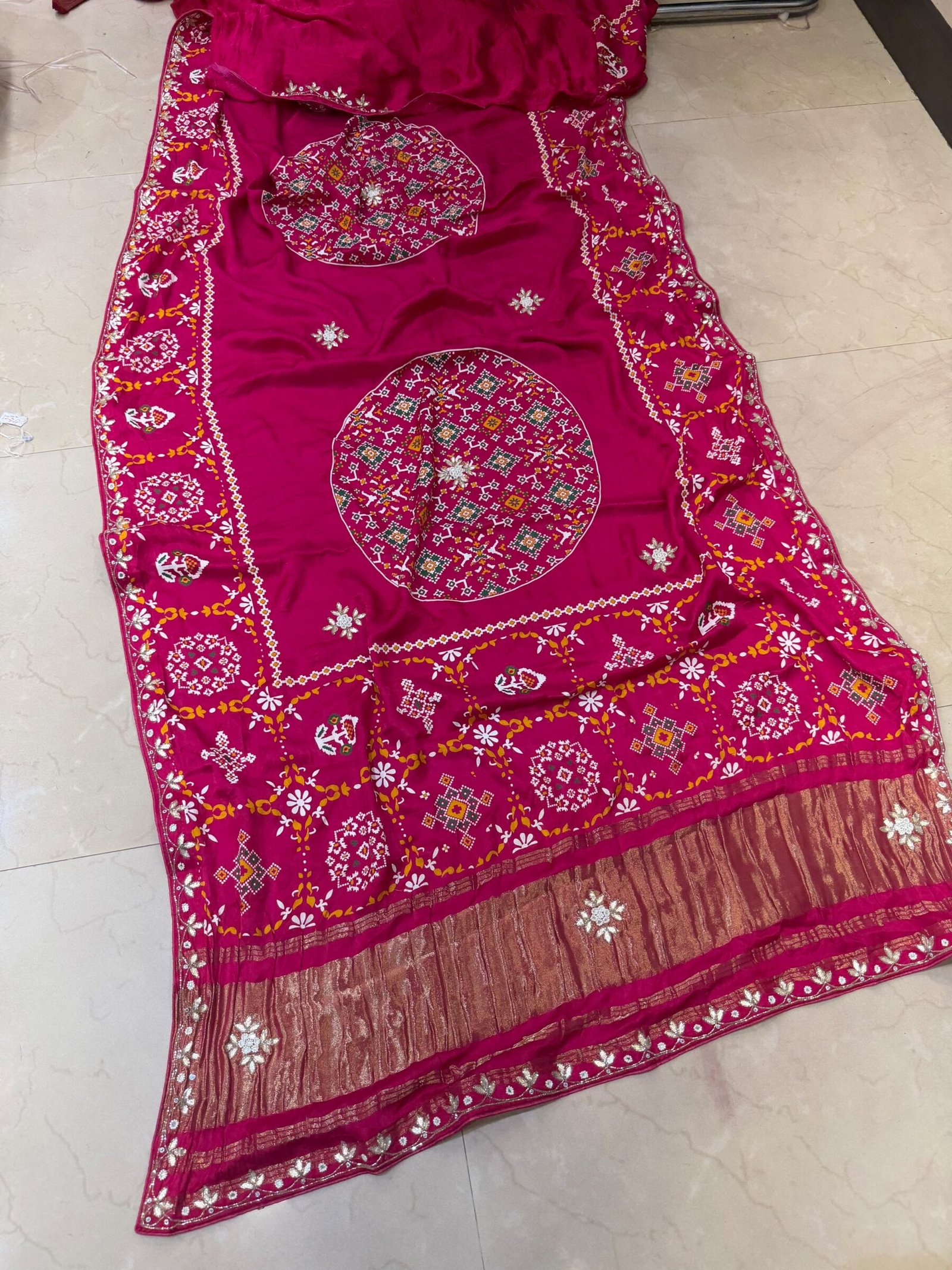 Pure Modal Gajji Patola Saree with Gota Patti Work 3 A beautiful red pure Modal Gajji Patola saree with intricate Gota Patti handwork and a metallic zari border spread across a tiled floor.