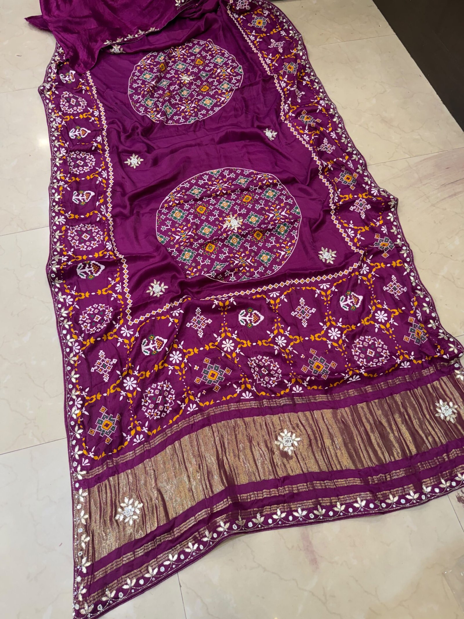 Pure Modal Gajji Patola Saree with Gota Patti Work 4 A beautiful red pure Modal Gajji Patola saree with intricate Gota Patti handwork and a metallic zari border spread across a tiled floor.