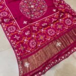 A beautiful red pure Modal Gajji Patola saree with intricate Gota Patti handwork and a metallic zari border spread across a tiled floor.