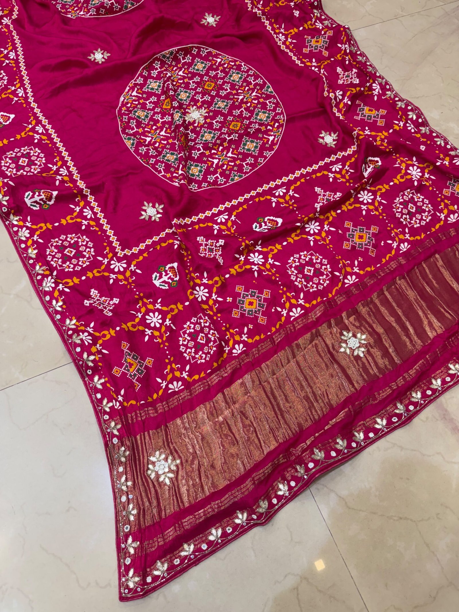 Pure Modal Gajji Patola Saree with Gota Patti Work 5 A beautiful red pure Modal Gajji Patola saree with intricate Gota Patti handwork and a metallic zari border spread across a tiled floor.