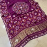 A beautiful red pure Modal Gajji Patola saree with intricate Gota Patti handwork and a metallic zari border spread across a tiled floor.