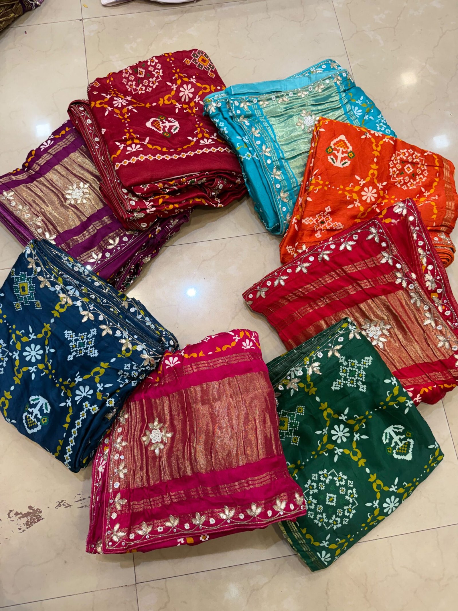 Pure Modal Gajji Patola Saree with Gota Patti Work 7 A beautiful red pure Modal Gajji Patola saree with intricate Gota Patti handwork and a metallic zari border spread across a tiled floor.