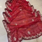 A red gajji silk bandhani saree with a heavy zari pallu and intricate hand Bandhej work laid out on a floor.