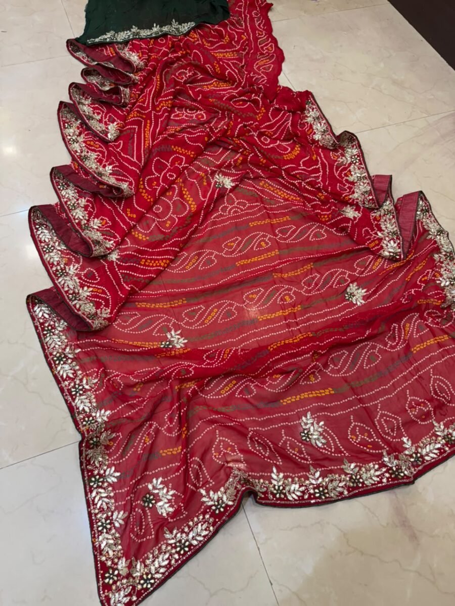 A red gajji silk bandhani saree with a heavy zari pallu and intricate hand Bandhej work laid out on a floor.