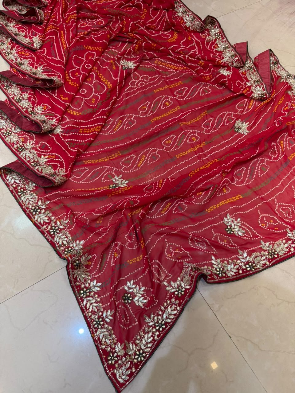 Gajji Silk Bandhani Saree with Heavy Zari Pallu 2 A red gajji silk bandhani saree with a heavy zari pallu and intricate hand Bandhej work laid out on a floor.