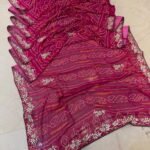 A red gajji silk bandhani saree with a heavy zari pallu and intricate hand Bandhej work laid out on a floor.