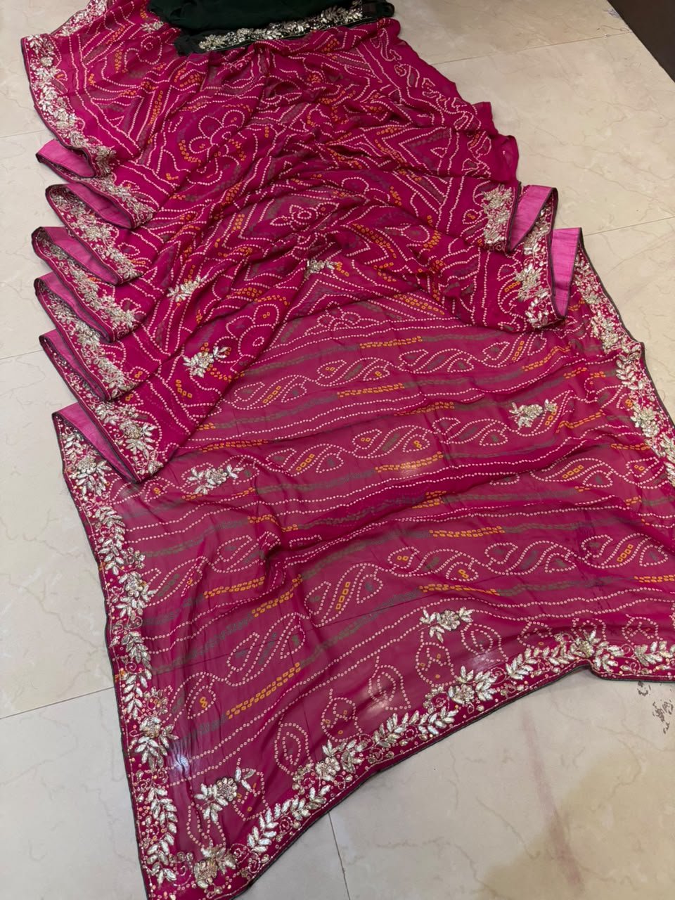 Gajji Silk Bandhani Saree with Heavy Zari Pallu 3 A red gajji silk bandhani saree with a heavy zari pallu and intricate hand Bandhej work laid out on a floor.