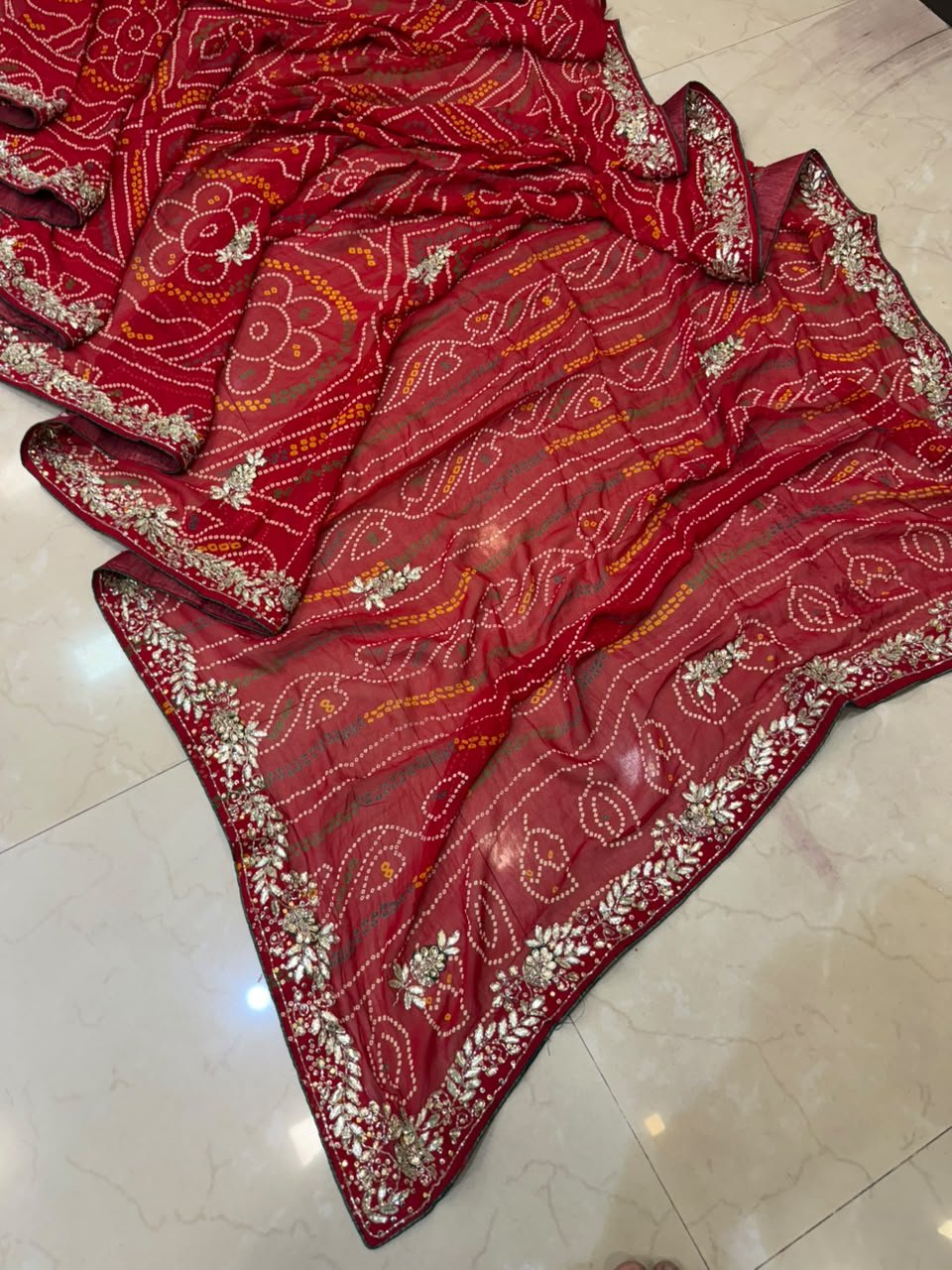 Gajji Silk Bandhani Saree with Heavy Zari Pallu 4 A red gajji silk bandhani saree with a heavy zari pallu and intricate hand Bandhej work laid out on a floor.