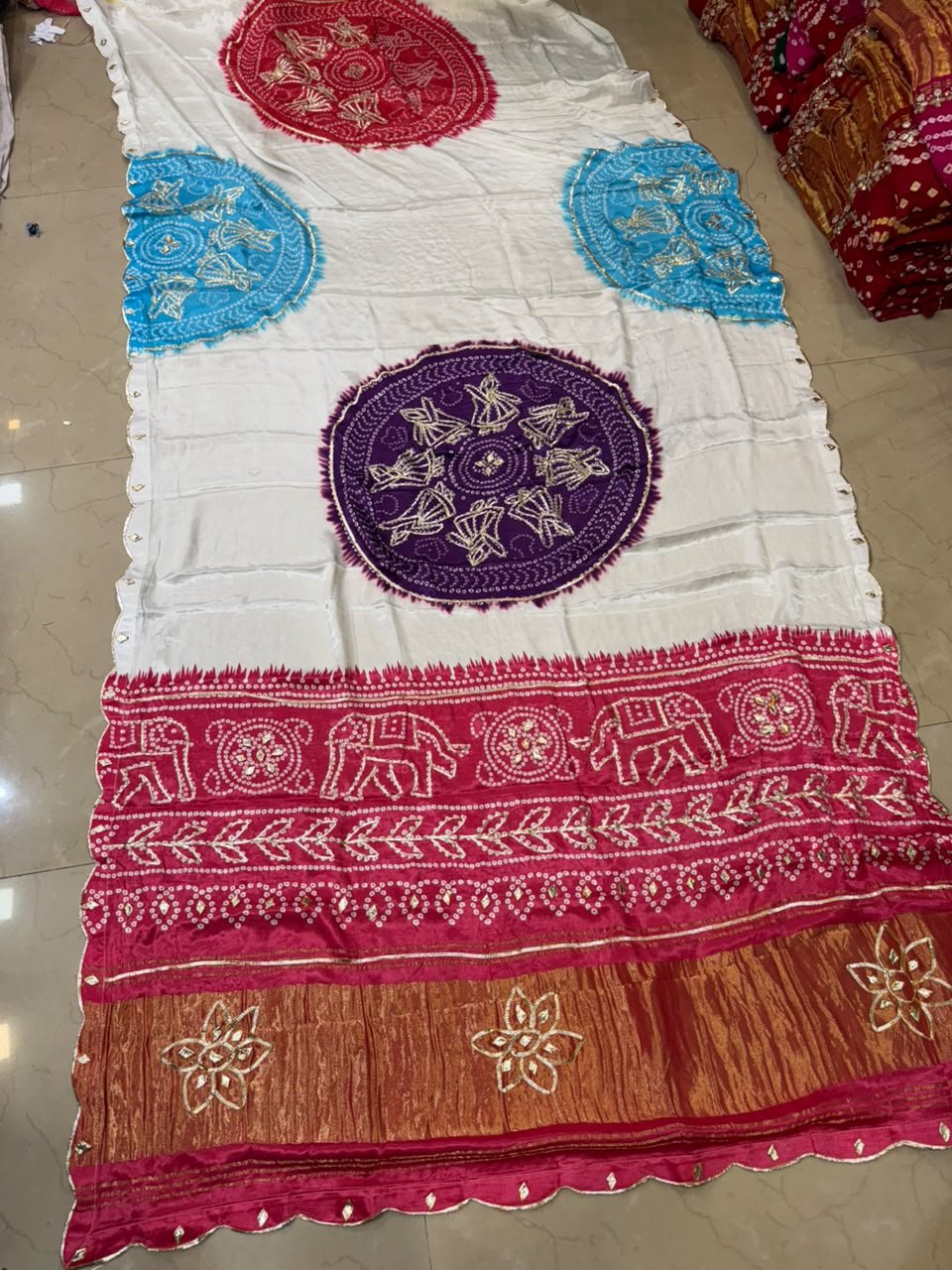 Pure Modal Gajji Silk Bandhej Saree with Gota Patti Work 3 A beautiful white and yellow Bandhej saree with a vibrant pink border featuring Gota Patti elephant and doll motifs.