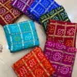 A collection of colorful gajji silk sarees with Bandhej patterns and zari checks laid out on a floor.
