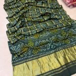 A collection of colorful gajji silk sarees with Bandhej patterns and zari checks laid out on a floor.
