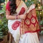 A woman wears a stunning white and red Gajji silk Bandhej saree with heavy Zari borders and intricate Gota Patti work.