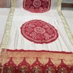 A woman wears a stunning white and red Gajji silk Bandhej saree with heavy Zari borders and intricate Gota Patti work.