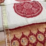 A woman wears a stunning white and red Gajji silk Bandhej saree with heavy Zari borders and intricate Gota Patti work.