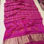 A collection of colorful gajji silk sarees with Bandhej patterns and zari checks laid out on a floor.