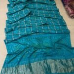 A collection of colorful gajji silk sarees with Bandhej patterns and zari checks laid out on a floor.