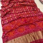 A collection of colorful gajji silk sarees with Bandhej patterns and zari checks laid out on a floor.