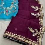 A beautiful deep purple Organza saree with detailed gold Gota patti handwork and a contrasting bright blue blouse piece.