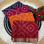 A flat lay of four colorful sarees featuring gold Gota Patti work and Nazbin Jacquard borders arranged on a white fur rug.
