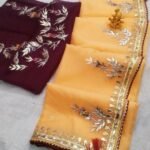 A beautiful deep purple Organza saree with detailed gold Gota patti handwork and a contrasting bright blue blouse piece.