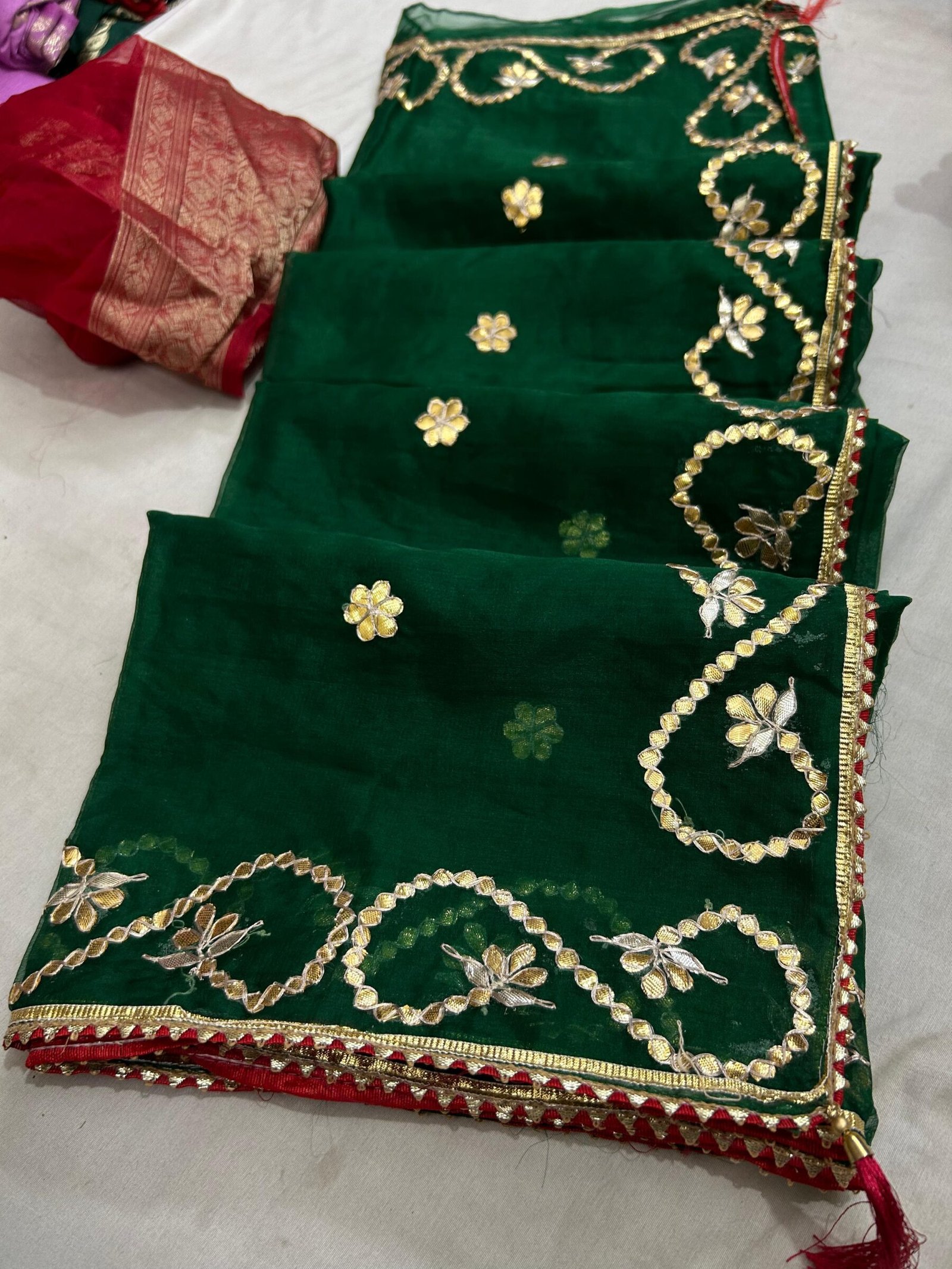 Elegant Organza Gota Patti Handwork Saree 3 A vibrant orange organza saree with intricate silver Gota Patti handwork laid out next to a deep red blouse piece.