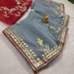 A beautiful deep purple Organza saree with detailed gold Gota patti handwork and a contrasting bright blue blouse piece.
