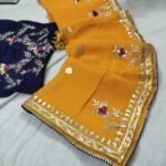 A beautiful deep purple Organza saree with detailed gold Gota patti handwork and a contrasting bright blue blouse piece.